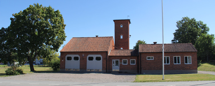 amla Uppsala brandstationsmuseum - en röd tegelbyggnad med vita garageportar och en flaggstång i förgrunden.