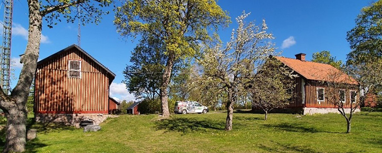 Nåntuna scoutgård - en rött trähus med stengrund. Der finns ett träd till vänster och tre till höger om huset.