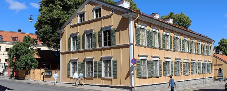 Walmstedska gården - en gul träbyggnad med vita knutar och gröna fönsterluckor.