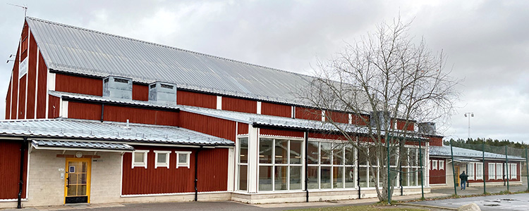 Almunge sim- och sporthall - en röd byggnad med vita knutar och förnsterfoder. Ett träd står framför.