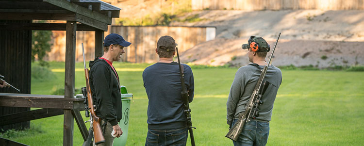 Ekebyboda skyttecentrum - tre män står vid en gräsmatta med gevär hängandes på ryggen.