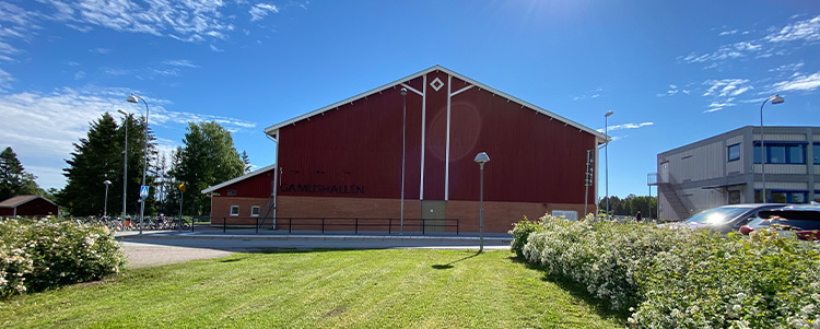 Gamla Uppsala sporthall - en röd byggnad med vita några detaljer. En gräsmatta och buskar i förgrunden.