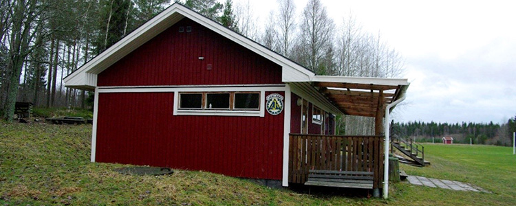 Järlåsa idrottsplats - ett rött klubbhus med vita knutar och till höger en fotbollsplan.
