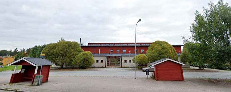 Vattholma sporthall, en röd och vit byggnad med träd på vardera sidan om entrén.